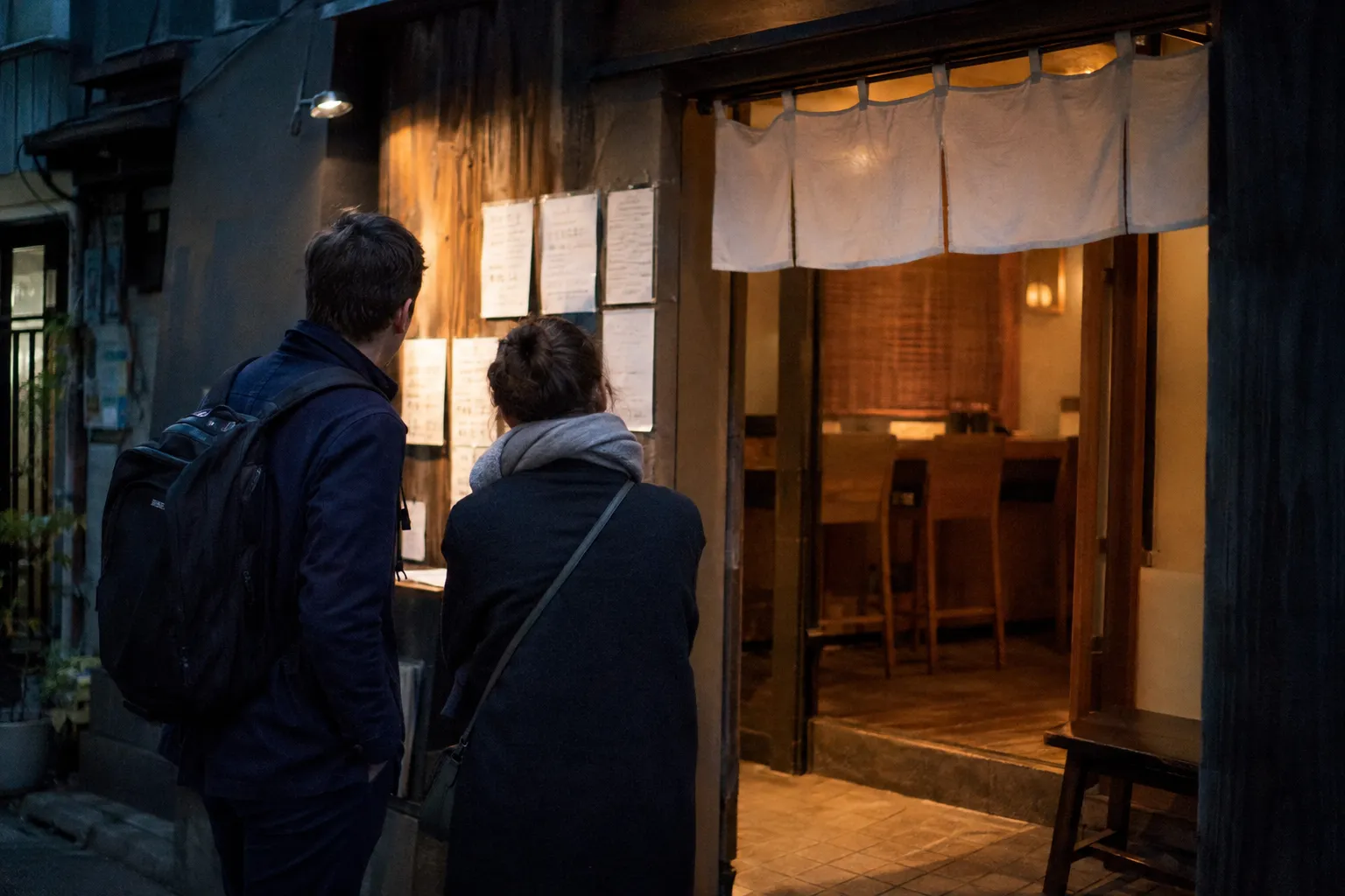 二人の旅行者が、店名のない小さな飲食店の前で、メニューと入口の段差を見て選ぶ様子。